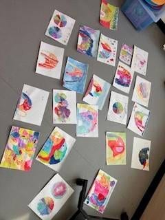bunte kinderkunstwerke, darunter abstrakte gemälde und farbraddesigns, sind auf dem grauen boden verstreut angeordnet.